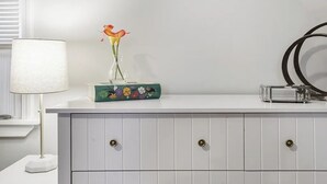 En vit byrå med en vas med blommor, en lampa och en dekorativ ask.