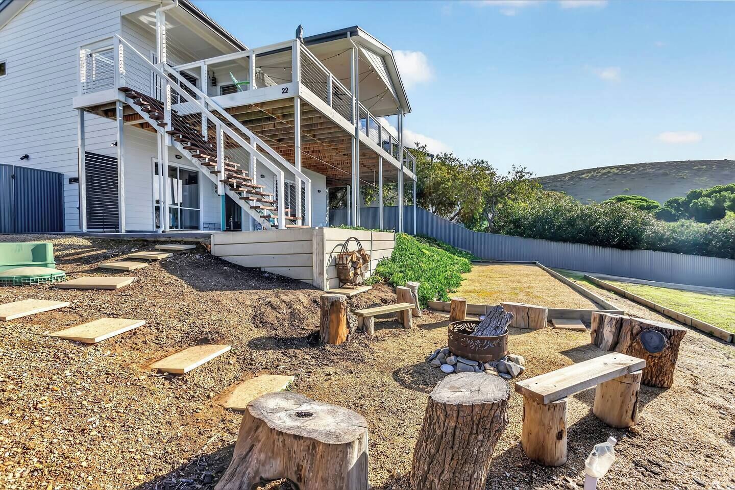 A modern house with a covered porch, a staircase, and a landscaped garden with wooden planters and a fire pit.