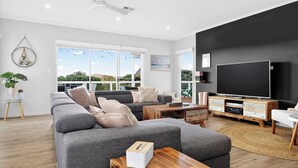 A modern living room with a large sofa, a coffee table, a TV, and a large window with a view. - The Ark Beachside Sanctuary with Valley Views (Second Valley)
