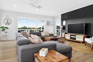 A modern living room with a large sofa, a coffee table, a TV, and a large window with a view. - The Ark Beachside Sanctuary with Valley Views (Second Valley)