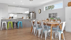 A modern kitchen with white cabinets, a wooden dining table, and colorful stools. - The Ark Beachside Sanctuary with Valley Views (Second Valley)