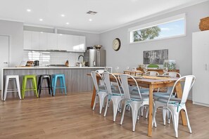 A modern kitchen with white cabinets, a wooden dining table, and colorful stools. - The Ark Beachside Sanctuary with Valley Views (Second Valley)