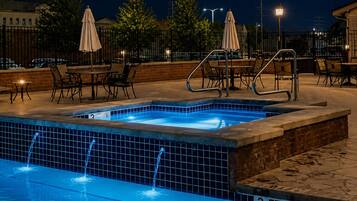 A swimming pool with a tiled edge, a lounge area with chairs and umbrellas, and a brick wall.