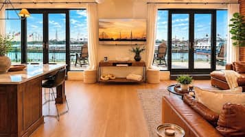 A spacious living area with a wooden floor, a sofa, a dining table, and large windows offering a view of a cityscape.