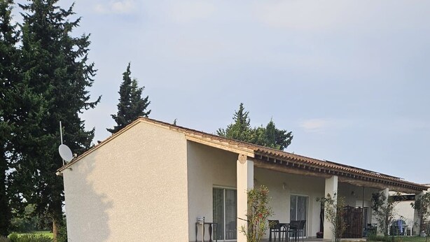 Ein Bungalow mit flachem Dach, einer überdachten Terrasse und einem gepflegten Rasen.
