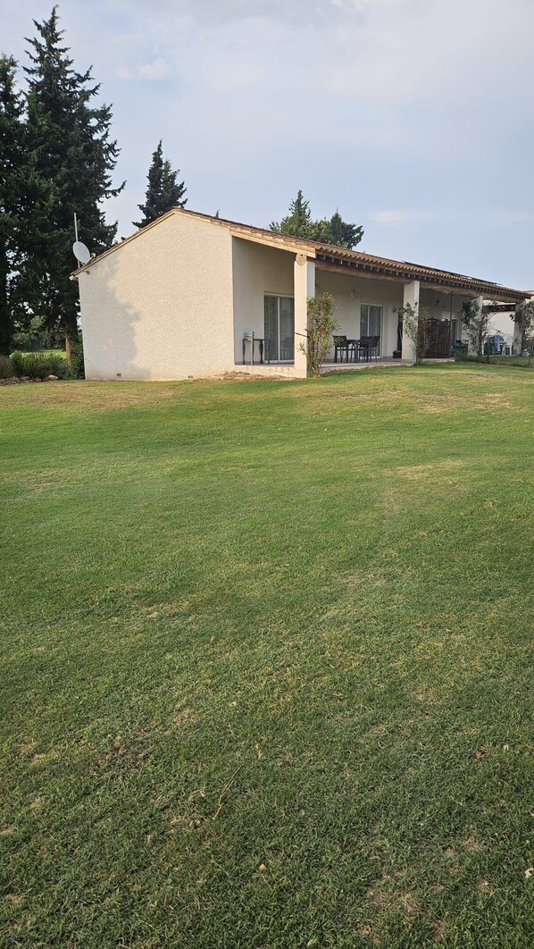 A single-story house with a flat roof, a covered patio area, and a well-maintained lawn.