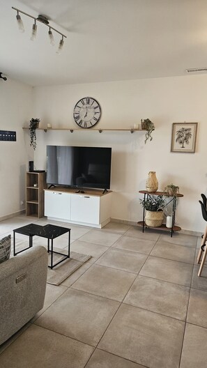 A living room with a flat-screen TV, a clock, and a shelf with decorative items.