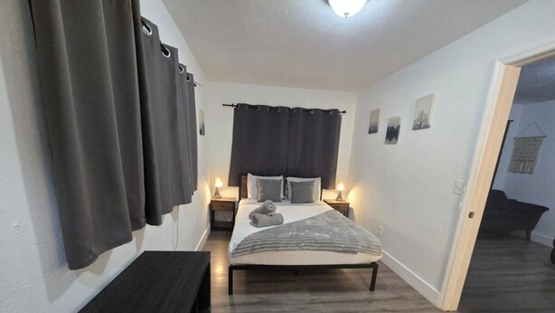 Ein Schlafzimmer mit einem Bett, Nachttischlampen, einer dunklen Holzbank und einer Tür zu einem anderen Raum.