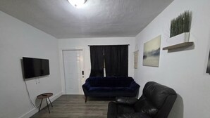 Ein Wohnzimmer mit Flachbildfernseher, Ledersessel, blauem Sofa, kleinem runden Tisch und einer Tür.