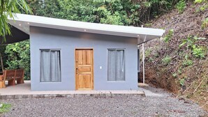 A modern, single-story building with a grey exterior, a wooden door, and two windows with curtains. - CASA MONO: Peace and Adventure (Pavones)