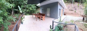 A modern building with a balcony, a wooden table and bench, and surrounding greenery.