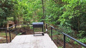 A concrete platform with a metal railing, a black grill, and a forested background. - CASA MONO: Peace and Adventure (Pavones)