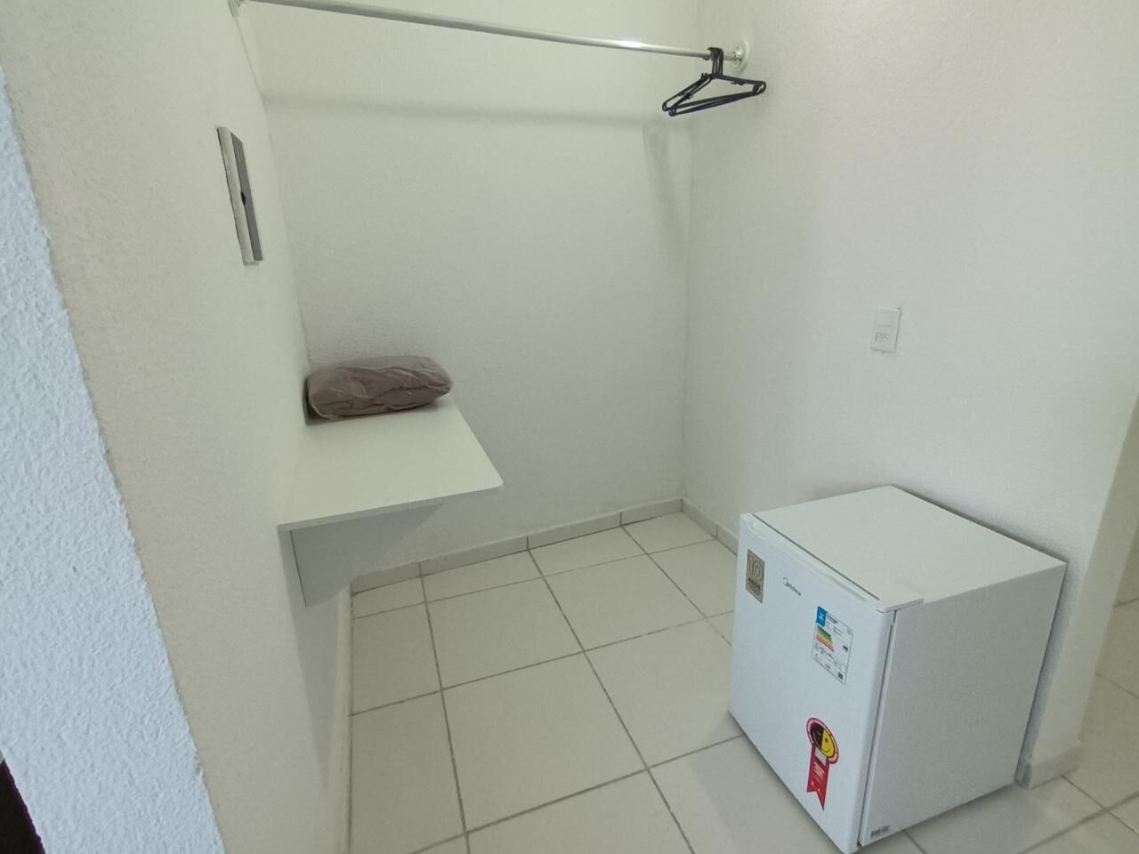 A small, white-walled room with a white tiled floor, a white cabinet with a towel, and a white refrigerator.