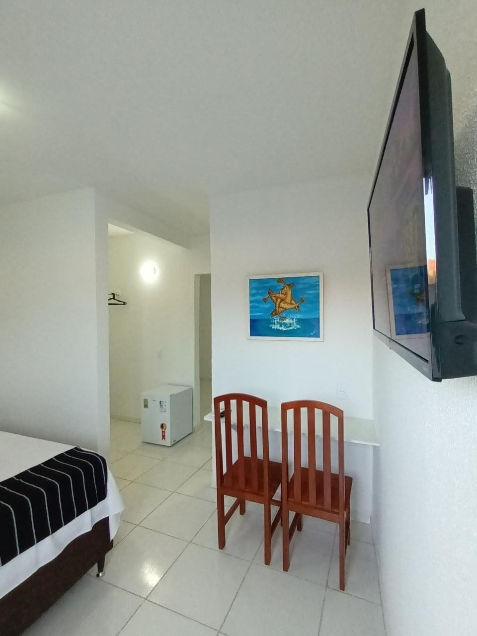 Una camera d'albergo con un letto, due sedie di legno, una televisione e un quadro appeso al muro.