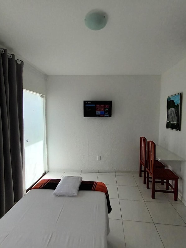 A hotel room with a bed, a desk, a chair, a TV, and a window with curtains.
