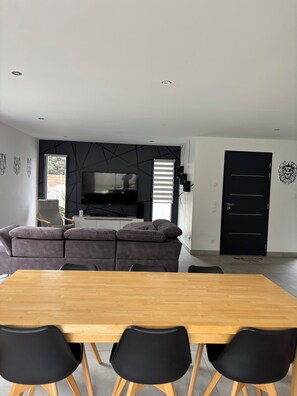 Ein modernes Wohnzimmer mit Sofa, Fernseher und Essbereich mit Holztisch und Stühlen.
