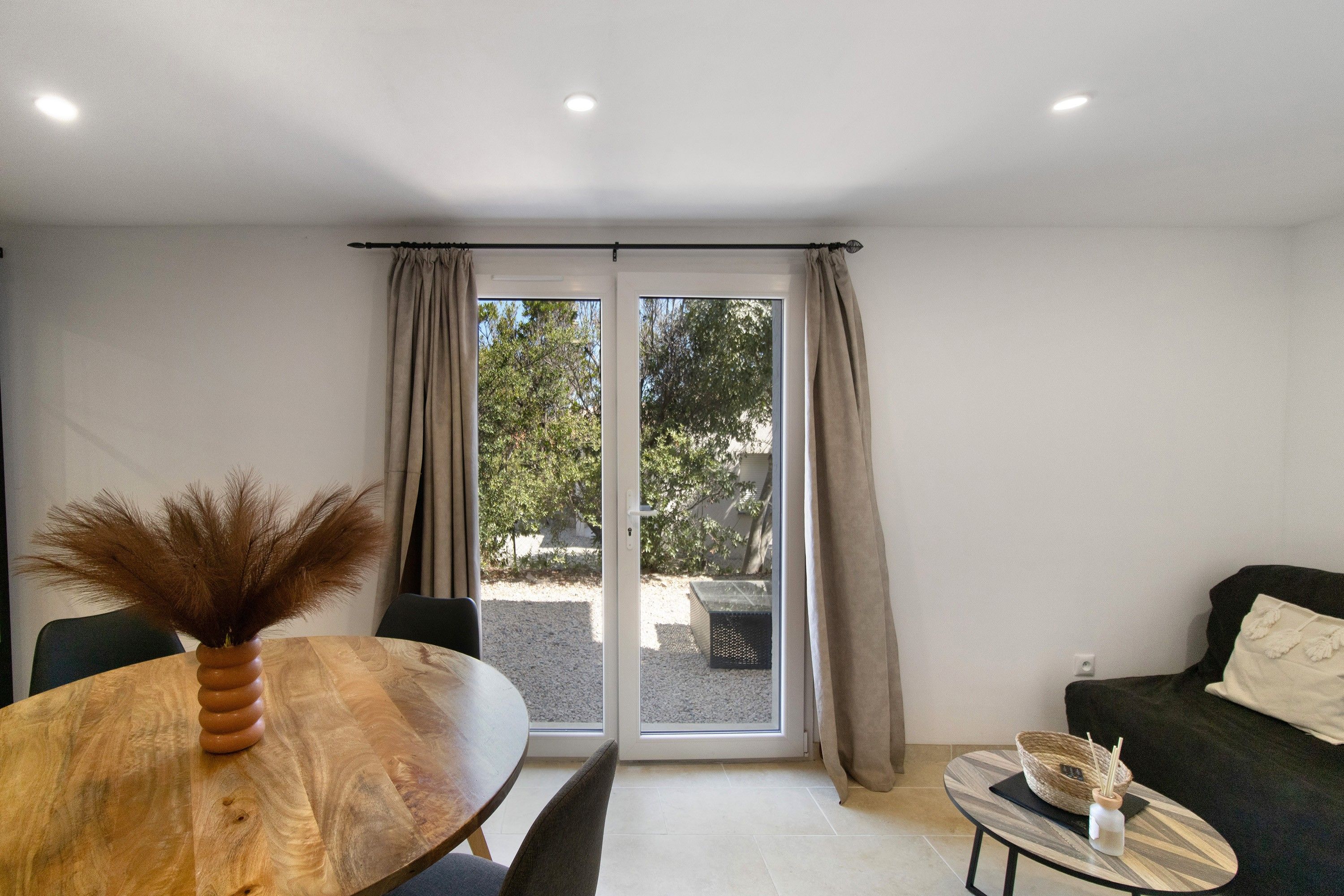 A room with a dining table, chairs, a sofa, and a window with curtains.