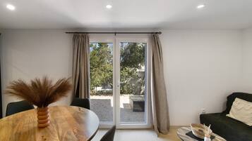 A room with a dining table, chairs, a sofa, and a window with curtains.