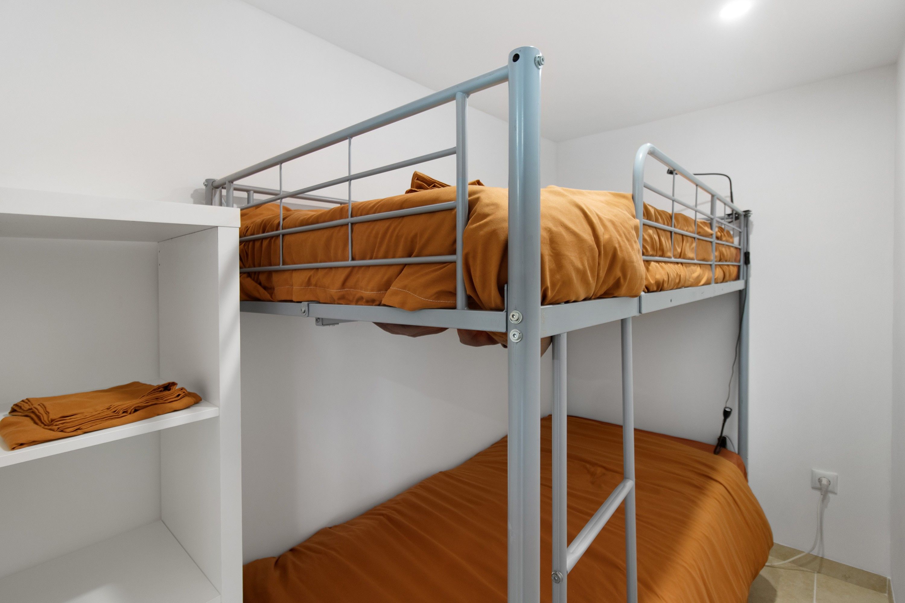 Un lit superposé avec une étagère en dessous et une prise électrique sur le mur.
