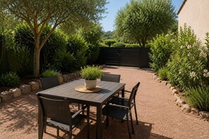 Een terras buiten met een tafel en stoelen, omringd door groen en een grindpad.
