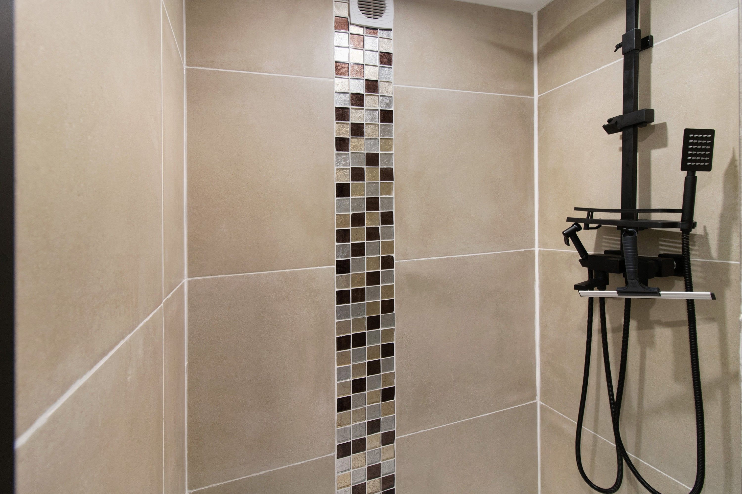 Un espace douche avec des carreaux de couleur beige et un motif décoratif en mosaïque verticale.