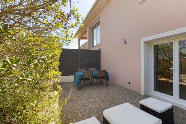 A patio area with a table and chairs, a small seating area, and a building with a window.