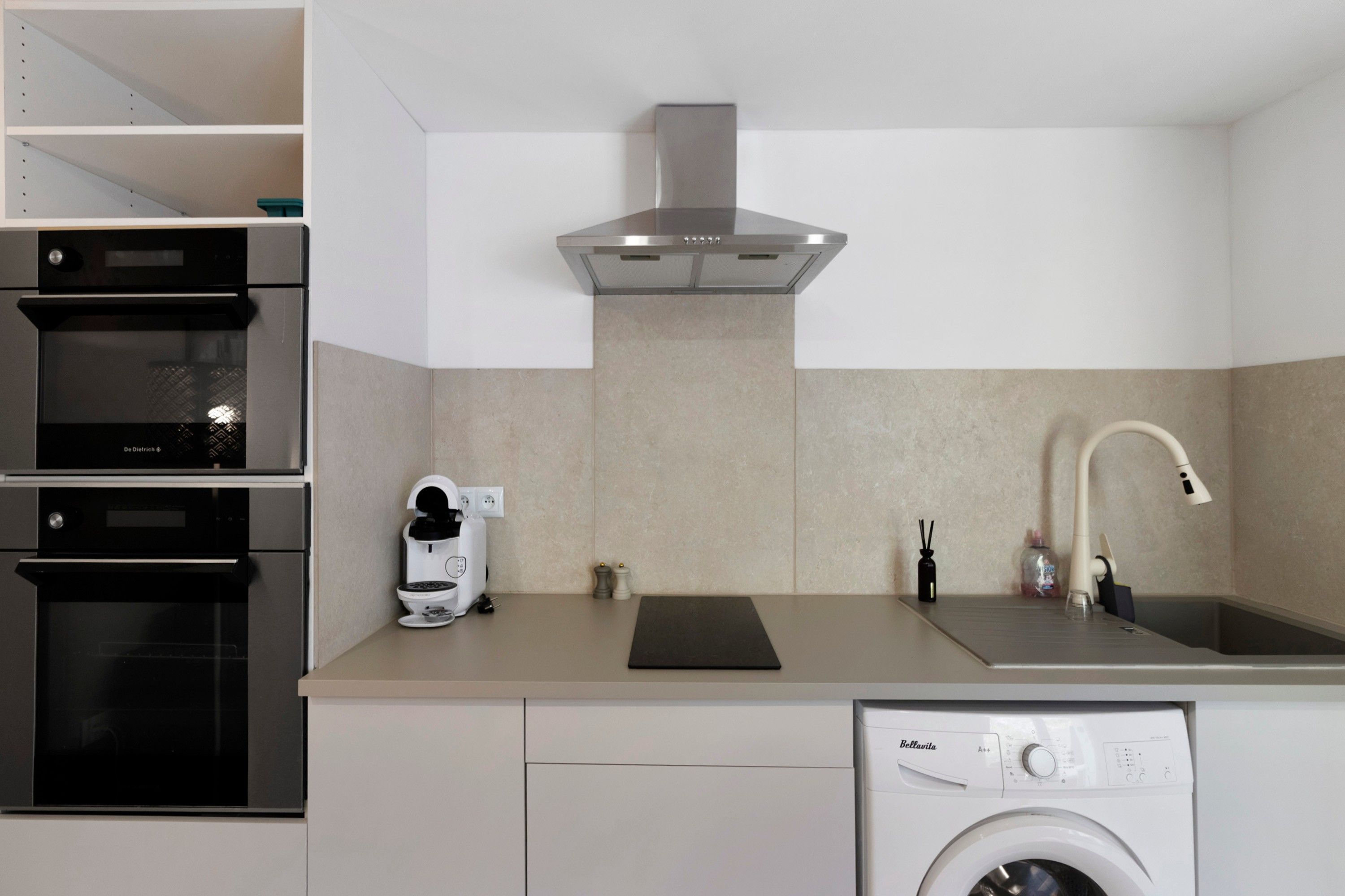 A modern kitchen with a built-in oven, a coffee machine, a sink, and a washing machine.