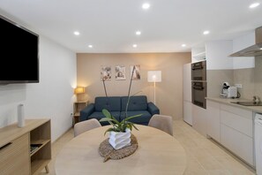 A modern living room with a sofa, a coffee table with a plant, and a flat-screen TV mounted on the wall.