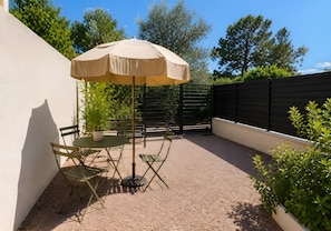 Un patio al aire libre con una mesa, sillas, un paraguas color beige y una planta en maceta.