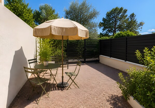 An outdoor patio with a table and chairs, a beige umbrella, and a potted plant. - Studio Apartment 'Villa Laurent' with Private Garden and Wi-Fi (Solaro)