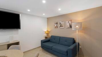 Sala de estar com sofá azul, TV de tela plana, abajur e três quadros na parede.