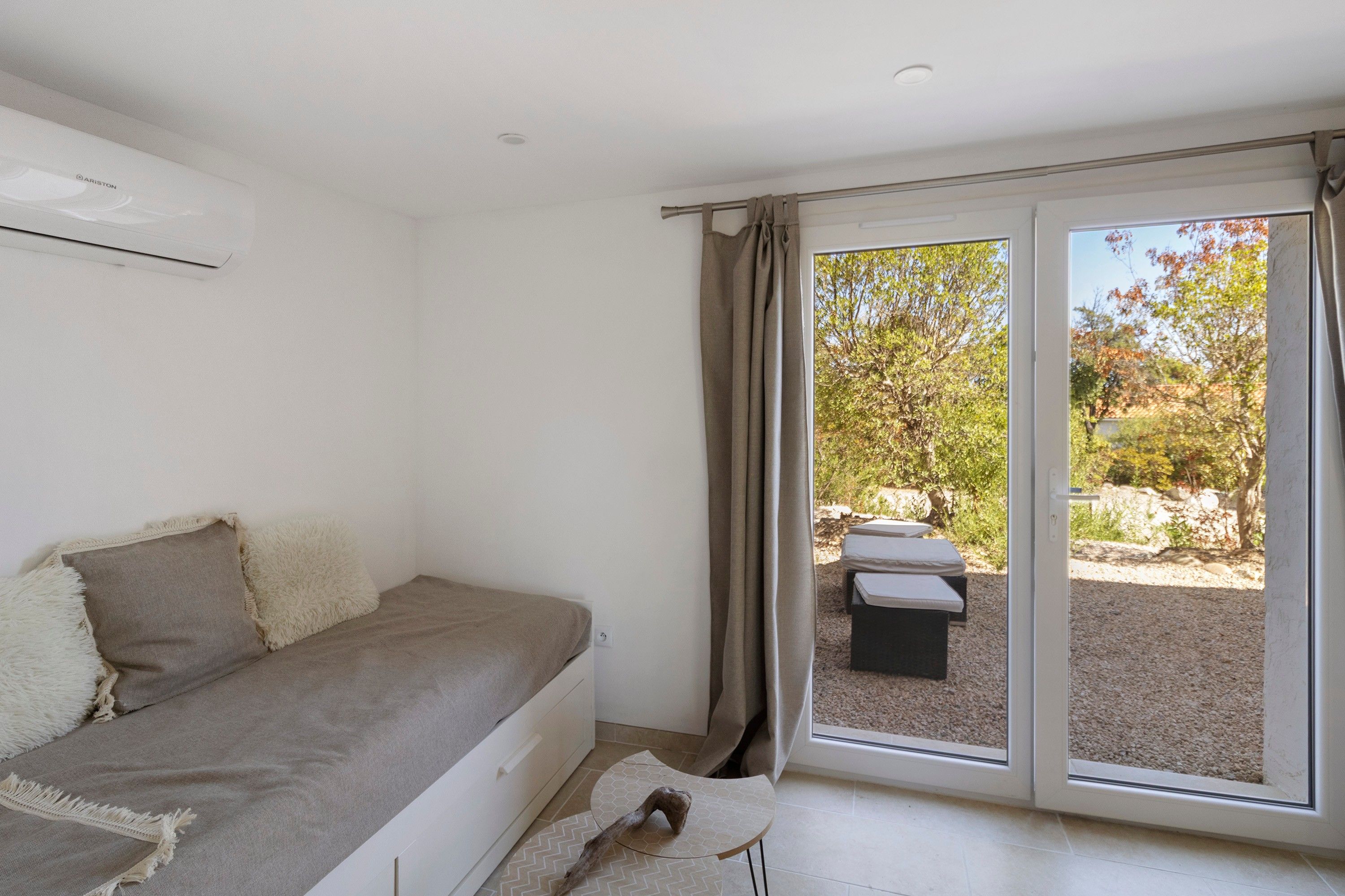Une chambre à coucher avec un lit, une fenêtre et une vue sur un espace extérieur aménagé avec une table et des chaises.