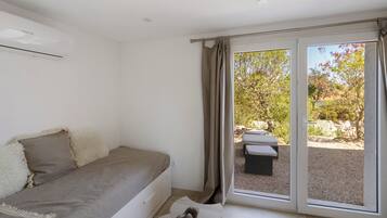 Une chambre à coucher avec un lit, une fenêtre et une vue sur un espace extérieur aménagé avec une table et des chaises.