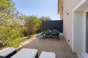 An outdoor seating area with a table and chairs, a covered table, and two lounge chairs.