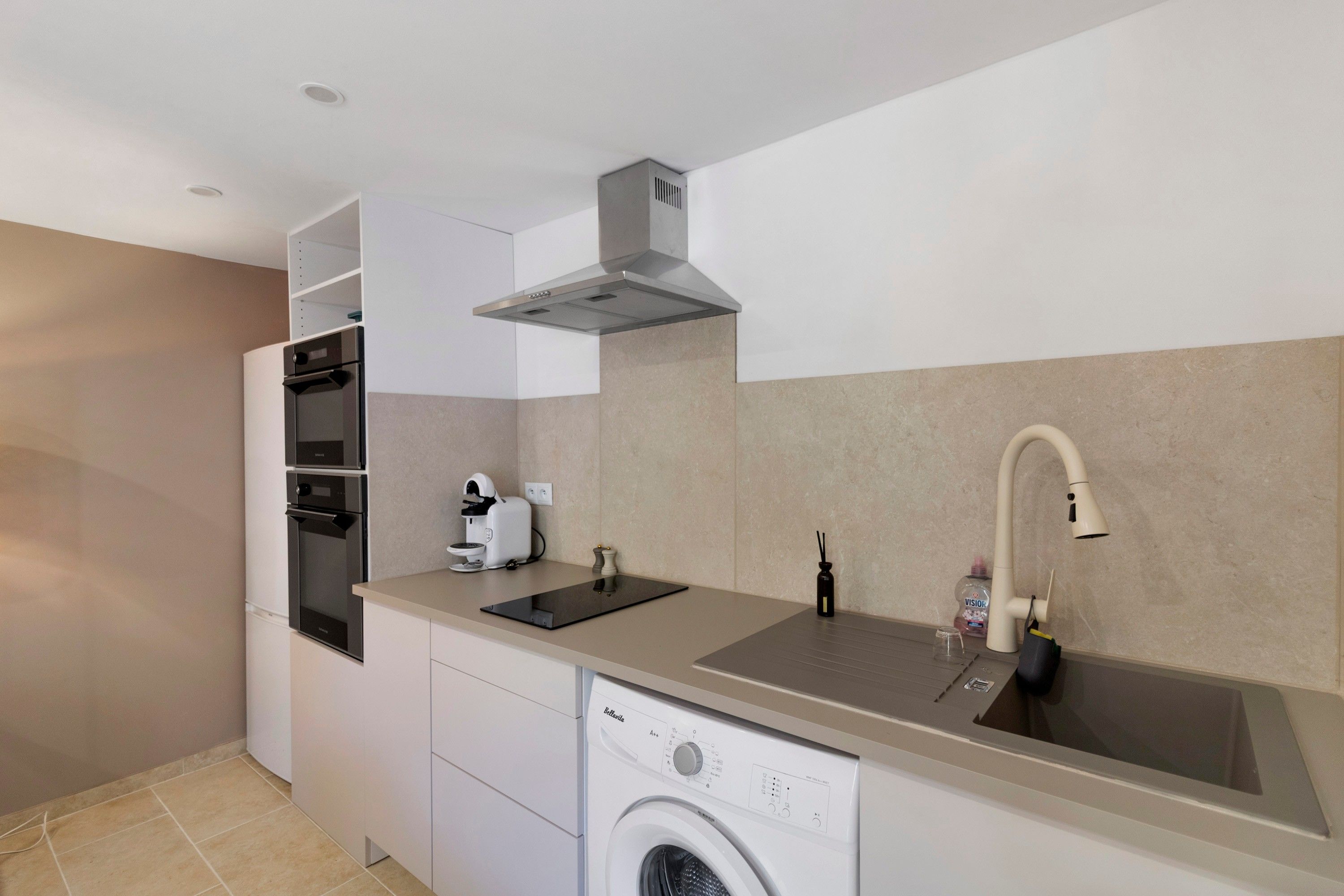 A compact kitchen with a built-in oven, a dishwasher, a sink, and a compact coffee maker.