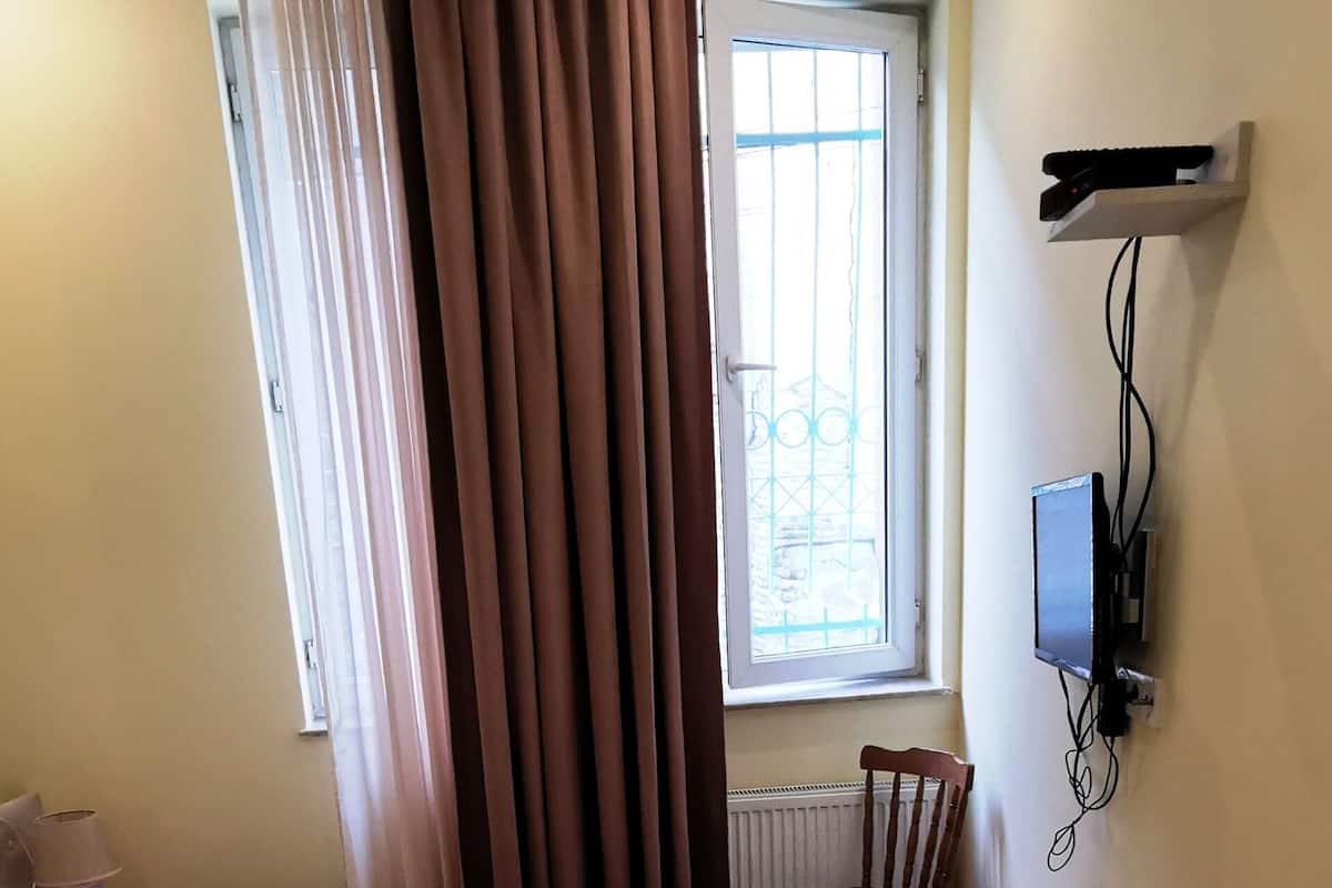 A hotel room with two beds, a chair, a window with curtains, a radiator, and a mounted TV.