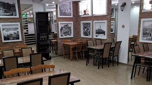 A spacious dining area with multiple tables and chairs, a brick wall with framed pictures, and a modern ceiling with recessed lighting. - Tbiliseli Inn (Tbilisi)
