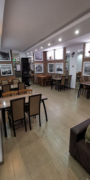 A spacious dining area with multiple tables and chairs, a brick wall with framed pictures, and a modern ceiling with recessed lighting. - Tbiliseli Inn (Tbilisi)