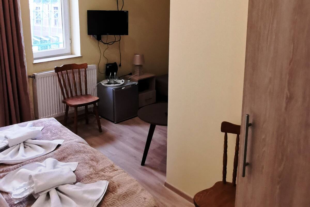 A bedroom with a bed, a desk, a chair, an air conditioning unit, and a window with curtains.