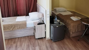 A compact hotel room with a bed, a small table, a refrigerator, and a bedside table with a lamp. - Tbiliseli Inn (Tbilisi)