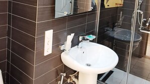 A modern bathroom with dark tiled walls, a white sink, a glass shower enclosure, and a mirror. - Tbiliseli Inn (Tbilisi)