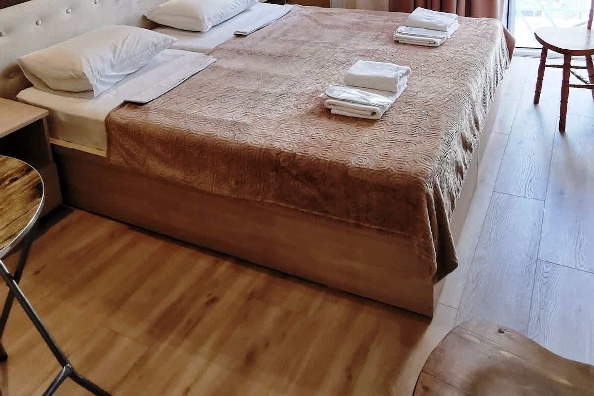 A hotel room with a large bed, a wooden floor, a small table, and a chair.