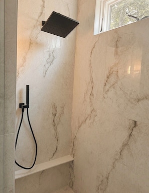 A bathroom with a shower, marble walls, and a window.