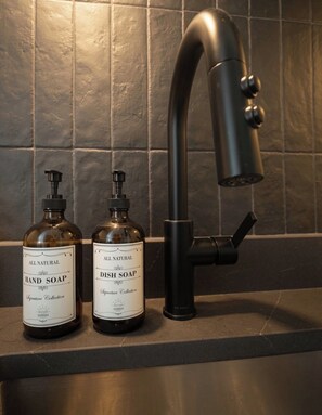 Two bottles of hand and dish soap on a kitchen counter with a modern faucet.