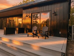Eine Holzterrasse mit Adirondack-Stühlen und einem schwarzen Tisch mit Blick auf einen Sonnenuntergang.