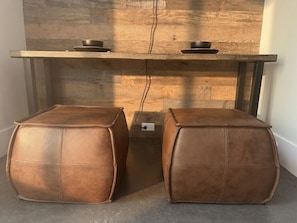 A wooden table with two black bowls on top, flanked by two brown leather poufs.