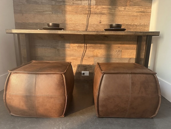 A wooden table with two black bowls on top, flanked by two brown leather poufs.