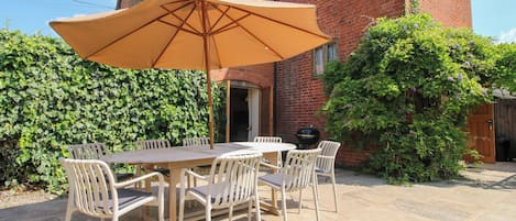 A patio with a table and chairs, a large umbrella, and a brick building in the background.