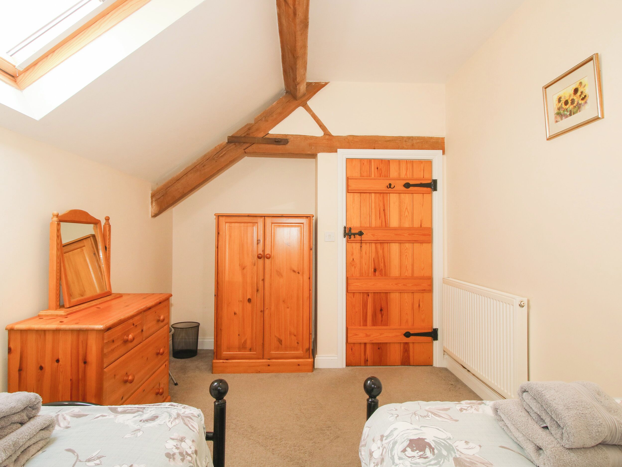 A bedroom with a sloped ceiling, wooden wardrobe, two beds, a mirror, and a radiator.