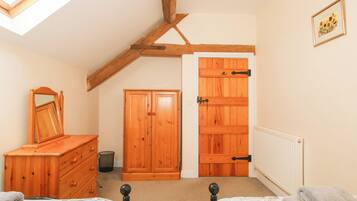 A bedroom with a sloped ceiling, wooden wardrobe, two beds, a mirror, and a radiator.